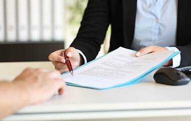 close up of an executive hands holding a pen and indicating where to sign a contract at office