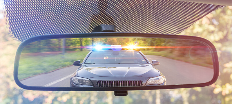 Police car with it's lights on through a rear view mirror