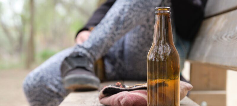 Person sitting on a bench next to an open bottle of beer