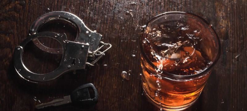 Glass of partially split liquor next to car keys and handcuffs