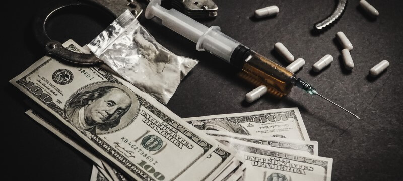 Drugs resting next to handcuffs and hundred dollar bills